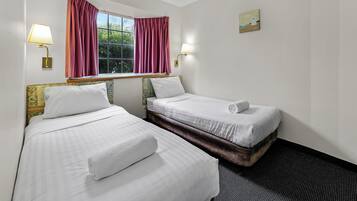 Una habitación de hotel con dos camas, una ventana con cortinas y dos lámparas fijadas a la pared.