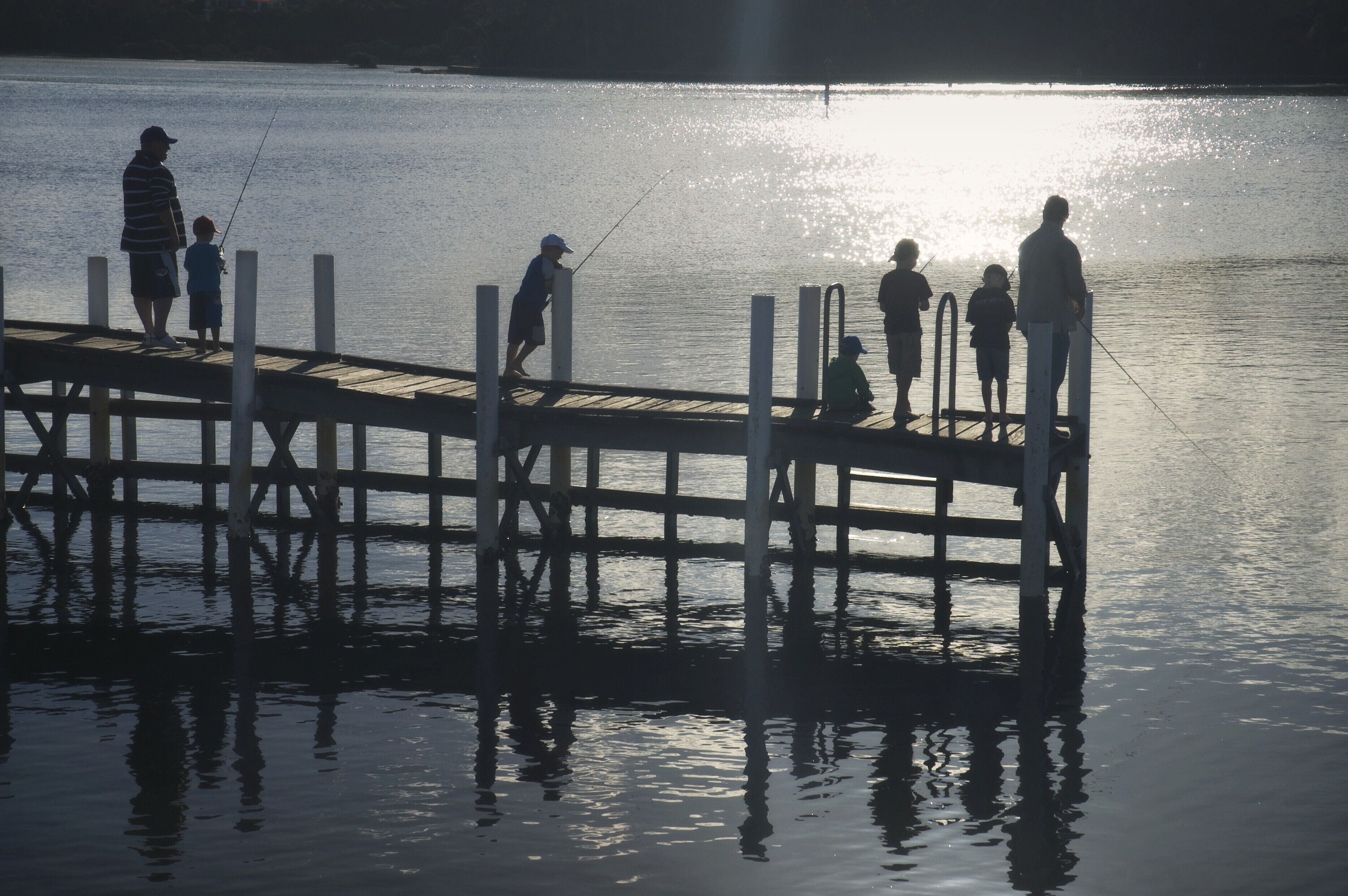 A wooden pier extending into calm water with people fishing.