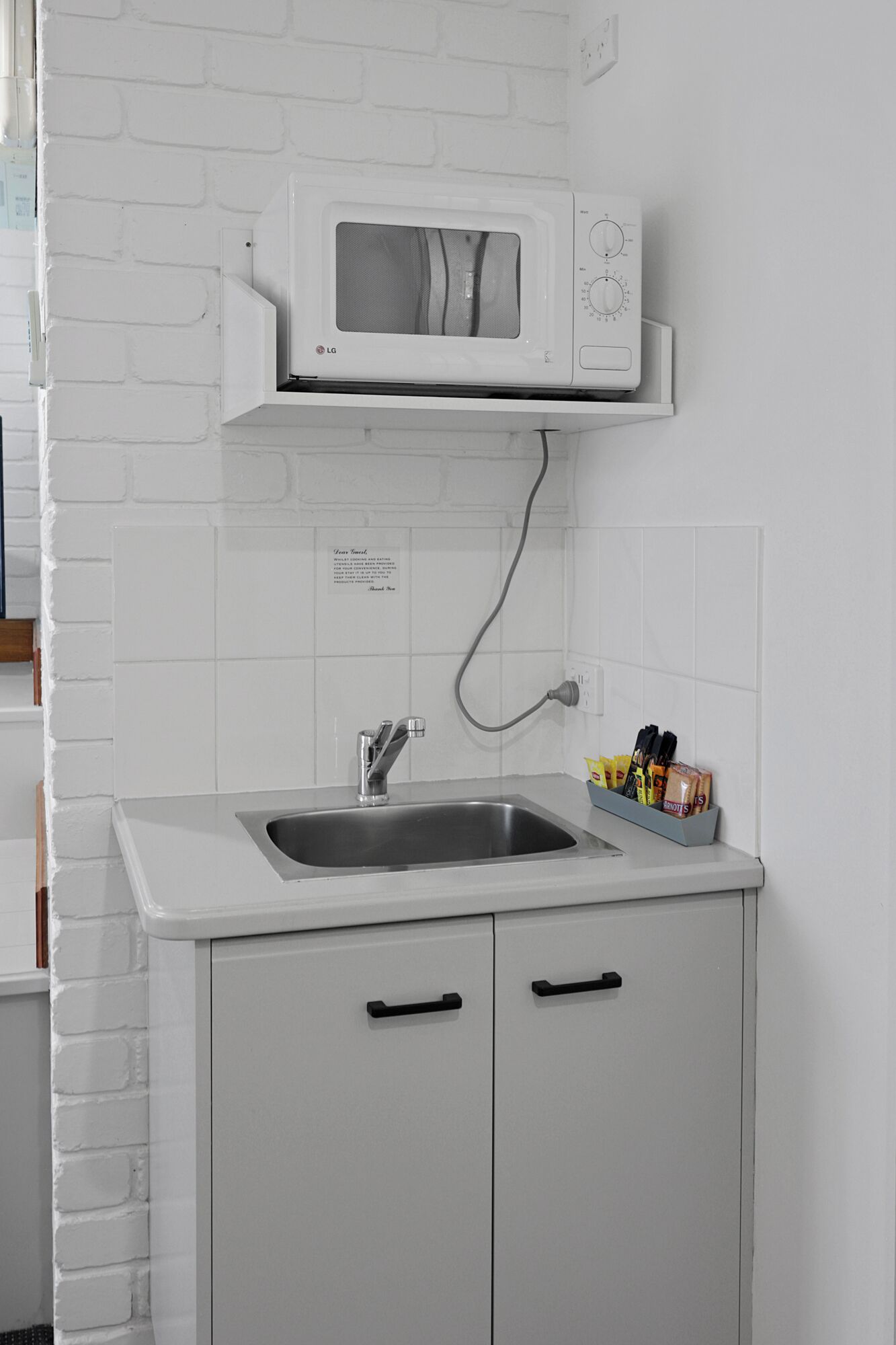 A kitchen with a white brick wall, a stainless steel sink, a microwave, and a spice rack.