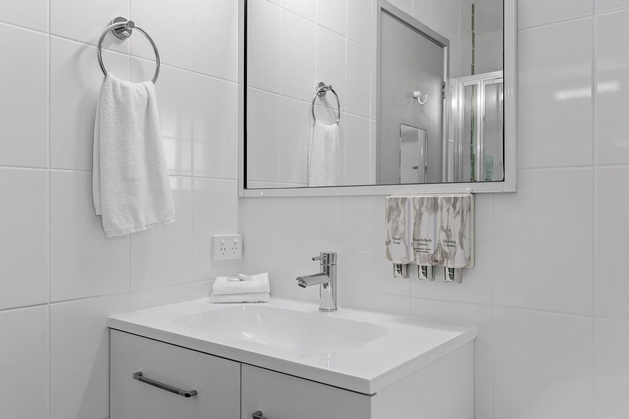 Een moderne badkamer met een wit wastafelmeubel, een spiegel en een handdoekrek.