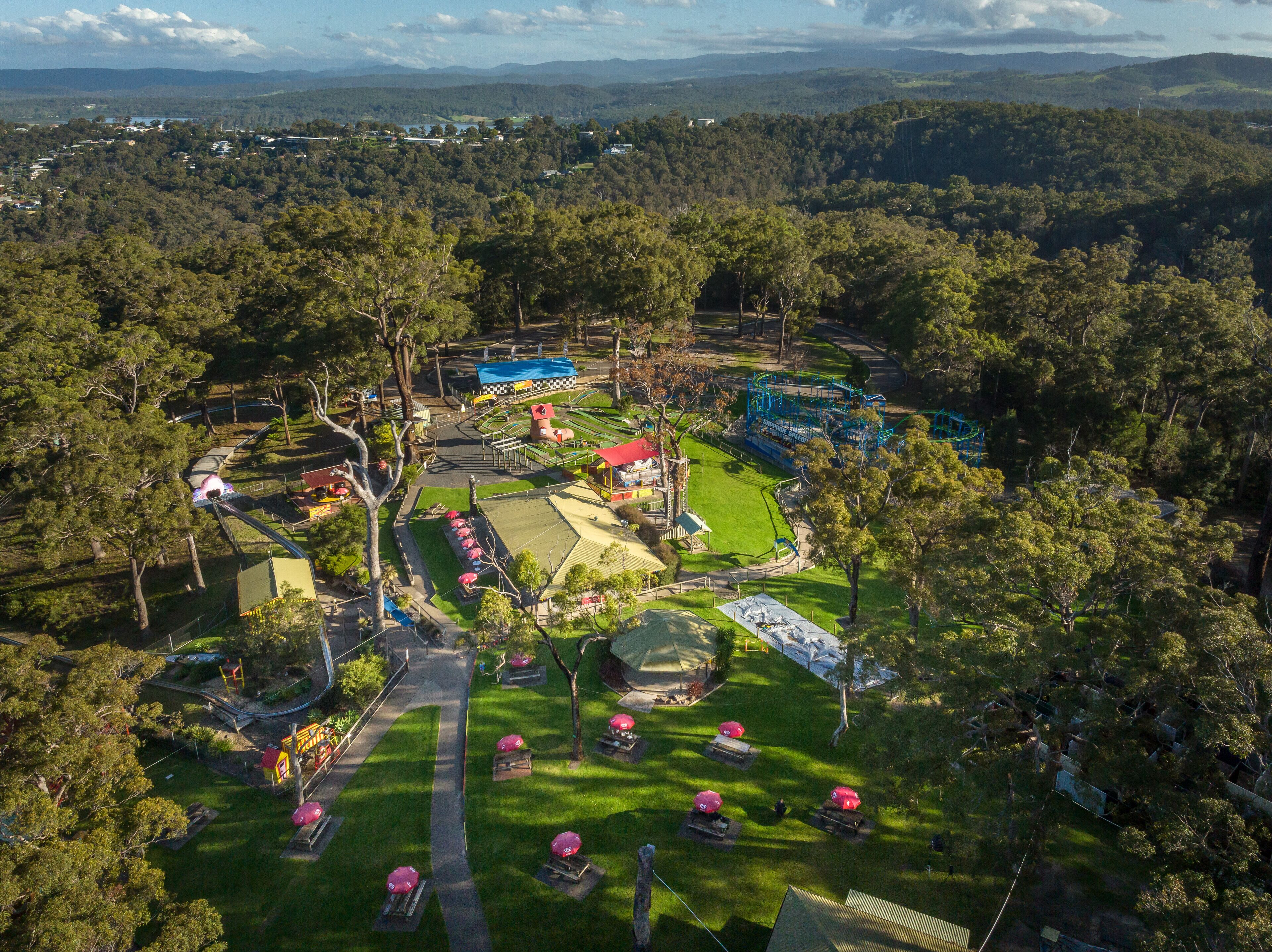 Vista aérea de un parque temático con montañas rusas, zonas de picnic y un lago.