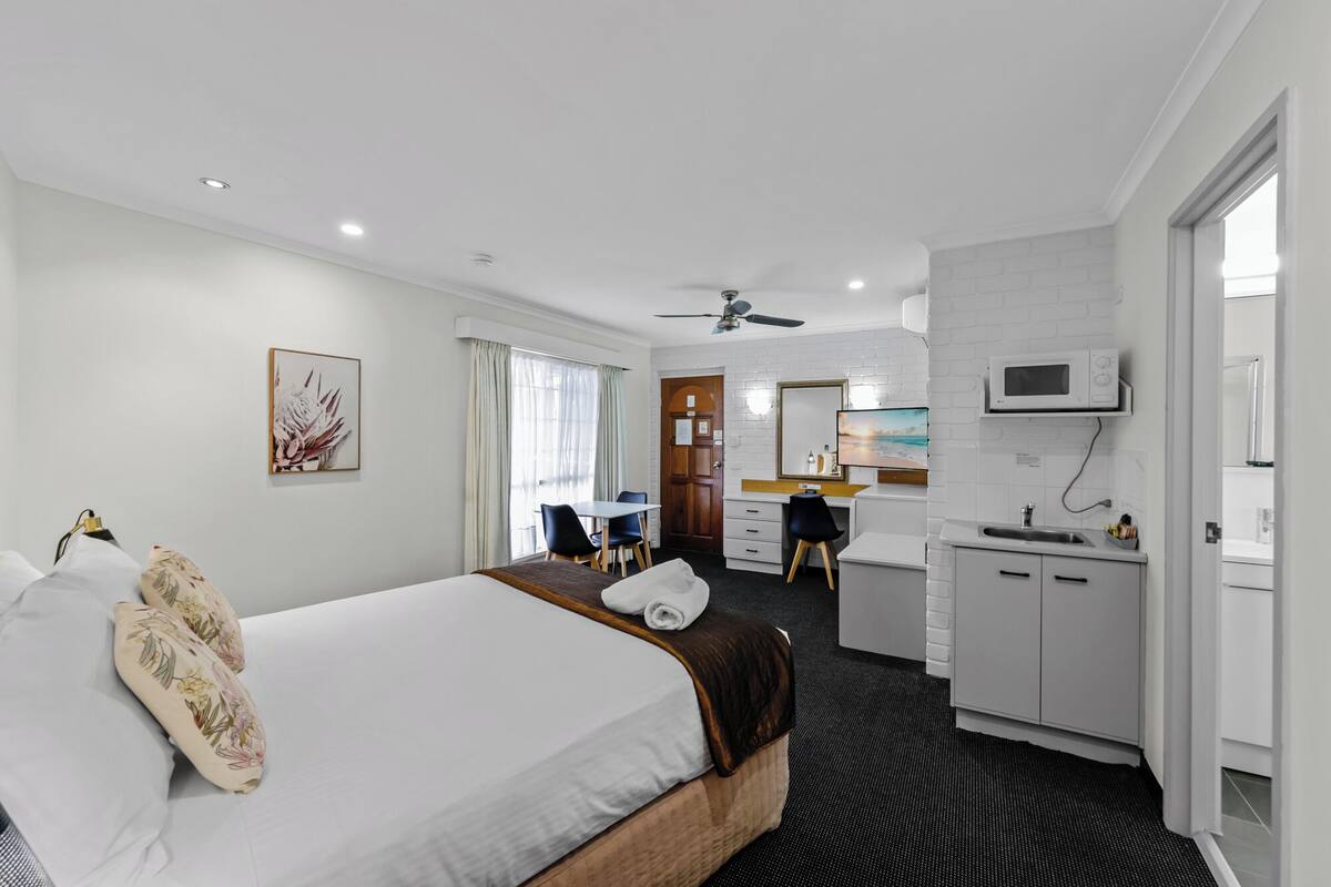 A hotel room with a bed, a desk, a kitchenette, and a bathroom.
