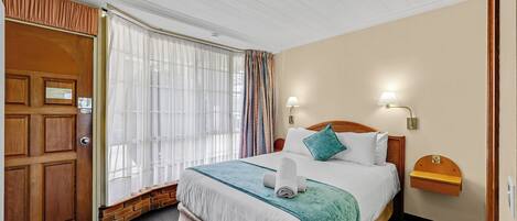 A hotel room with a wooden door, a large bed with a teal bedspread, white bedding, and two wall-mounted lamps.