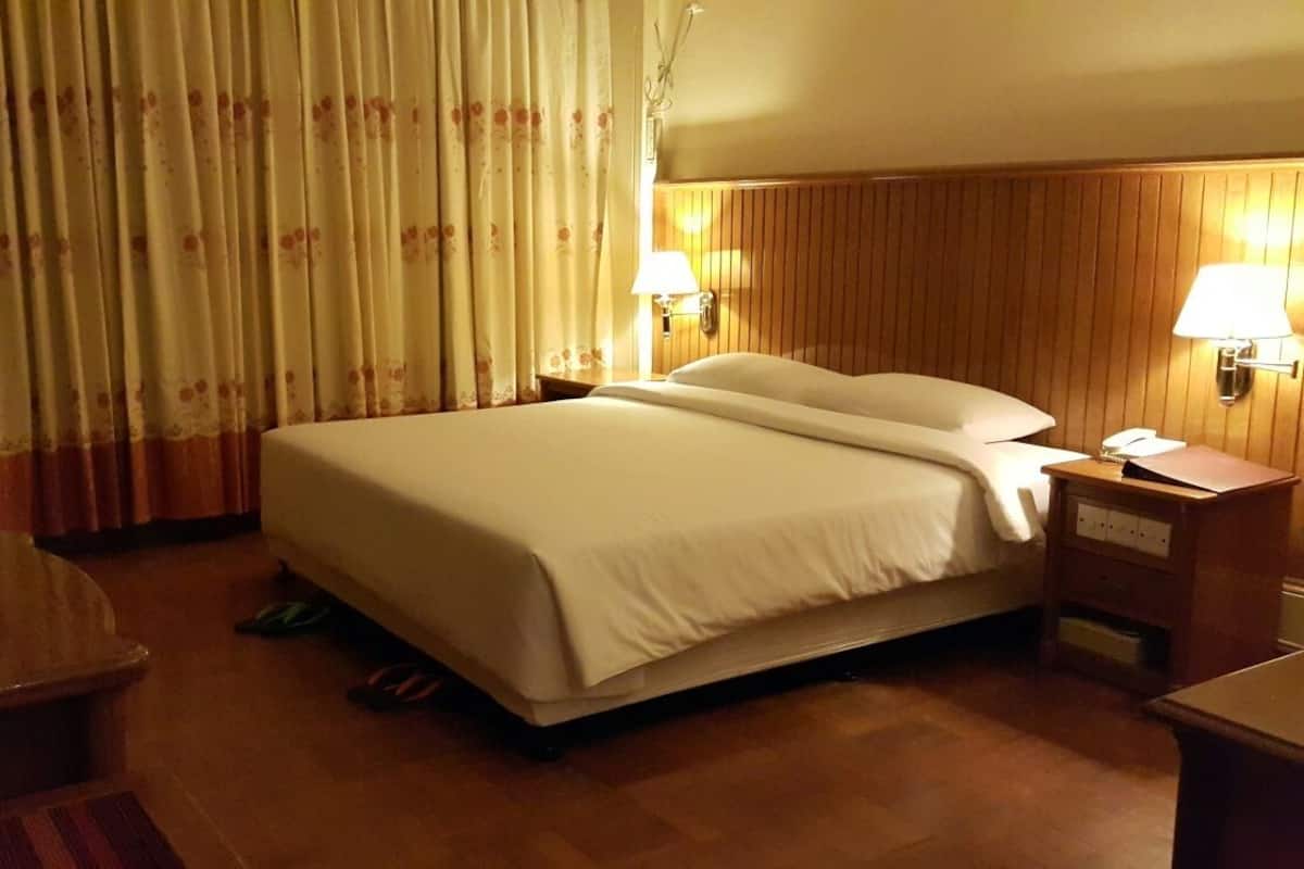A hotel room with a large bed, wooden headboard, two bedside lamps, a flat-screen TV, and a wooden nightstand.