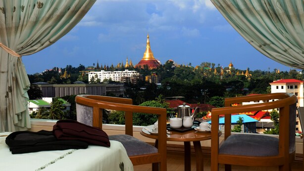 Habitación de hotel con balcón que ofrece vistas a un paisaje urbano, destacando un pagodas dorado y edificios circundantes.