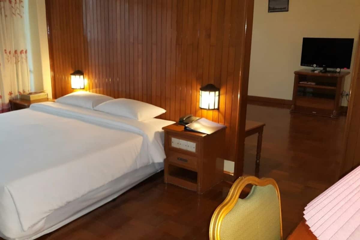 A hotel room with a large bed, wooden headboard, two bedside lamps, a wooden nightstand, a television on a stand, and a chair.