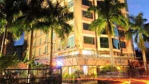 Un hotel de varios pisos con un letrero llamativo, balcones y palmeras en la parte delantera.