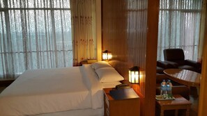 Habitación de hotel con una cama grande, dos lámparas de noche, una mesita con una botella y un plato, y una silla.