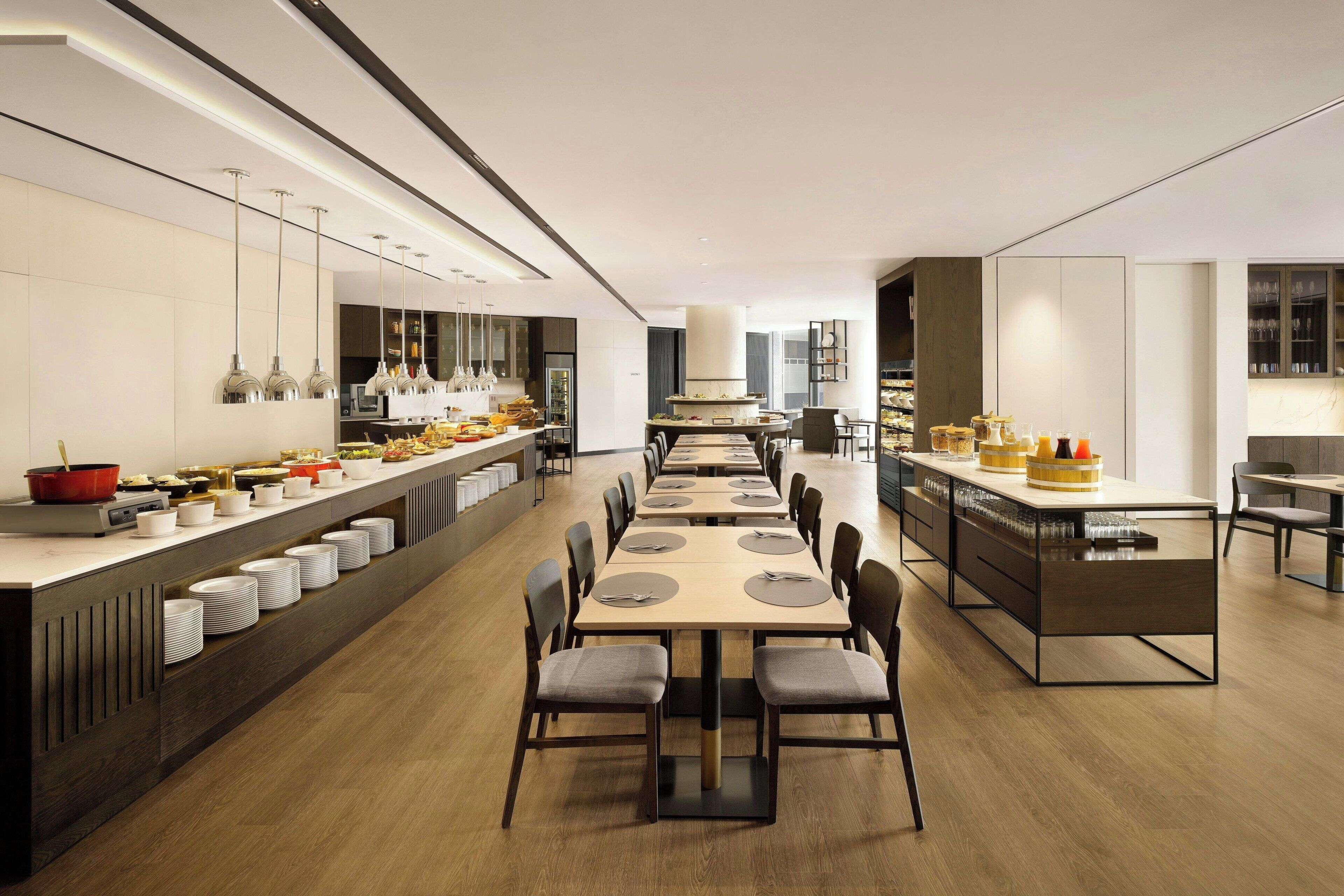 A modern dining area with long tables, chairs, and a buffet setup.