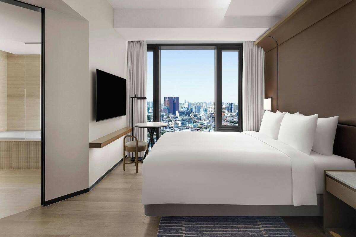 Une chambre d’hôtel moderne avec un grand lit, une télévision, une vue sur la ville et une petite table.