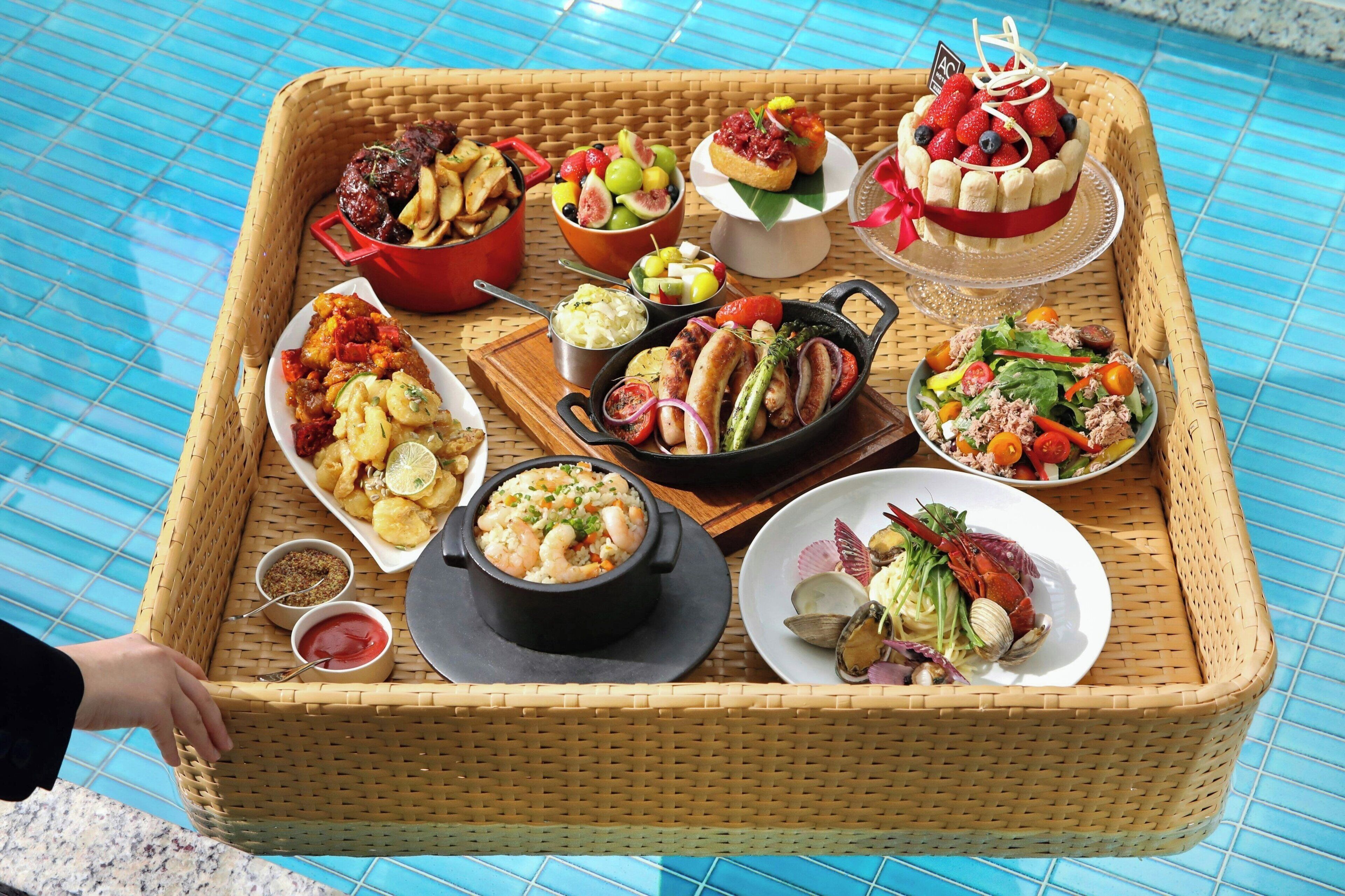 A variety of dishes arranged on a woven tray by a poolside.