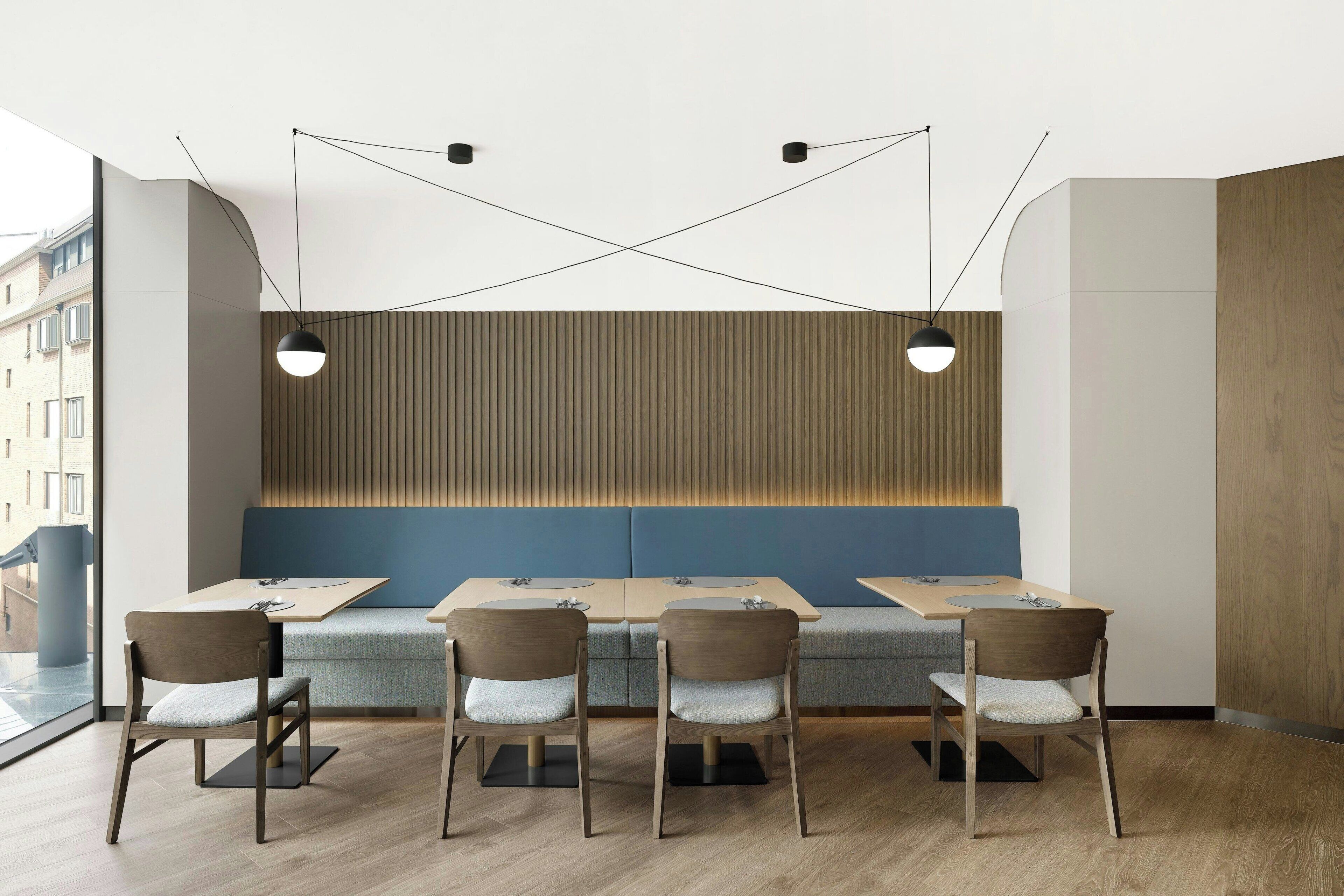 Un interior de restaurante moderno con suelo de madera, asientos acolchados azules e iluminación colgante negra.
