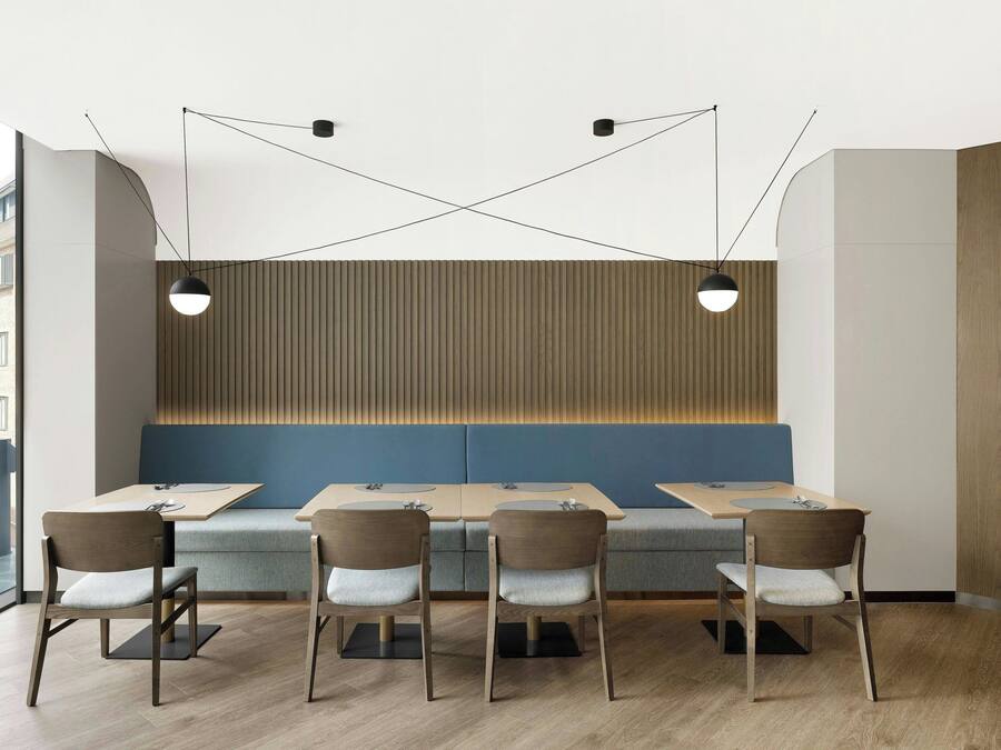 Un interior de restaurante moderno con suelo de madera, asientos acolchados azules e iluminación colgante negra.
