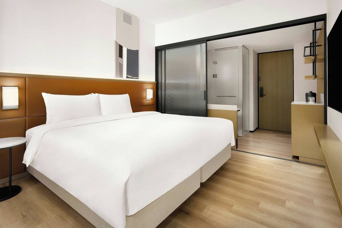 Une chambre d’hôtel moderne avec un grand lit, une table de chevet et une armoire avec un miroir.