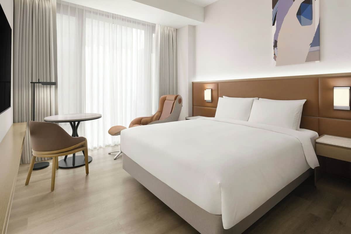 Une chambre d’hôtel moderne avec un grand lit, une chaise, une petite table et un téléviseur.