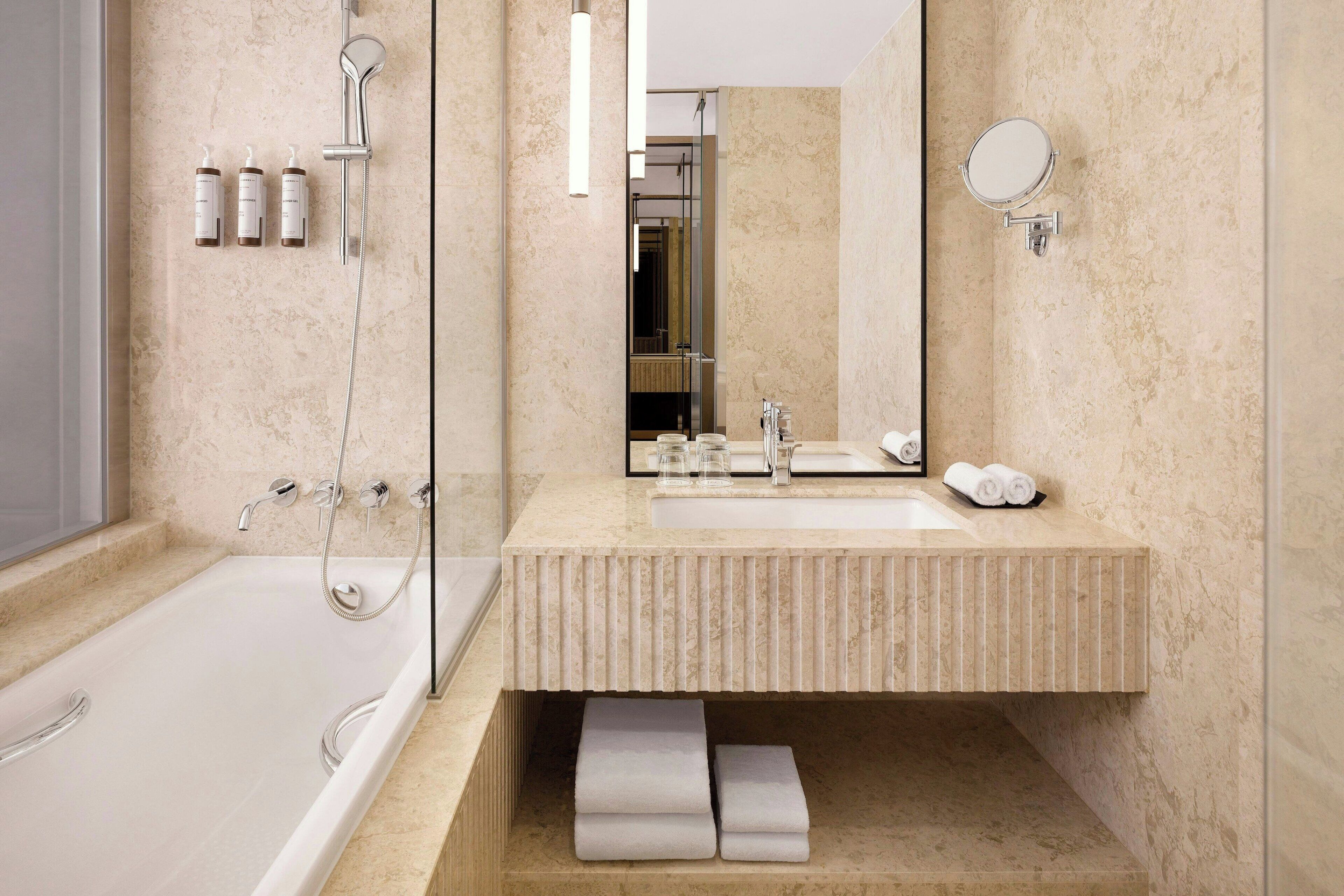 Une salle de bain moderne avec une baignoire, un lavabo et un miroir. On trouve des serviettes et des articles de toilette sur le comptoir du lavabo.