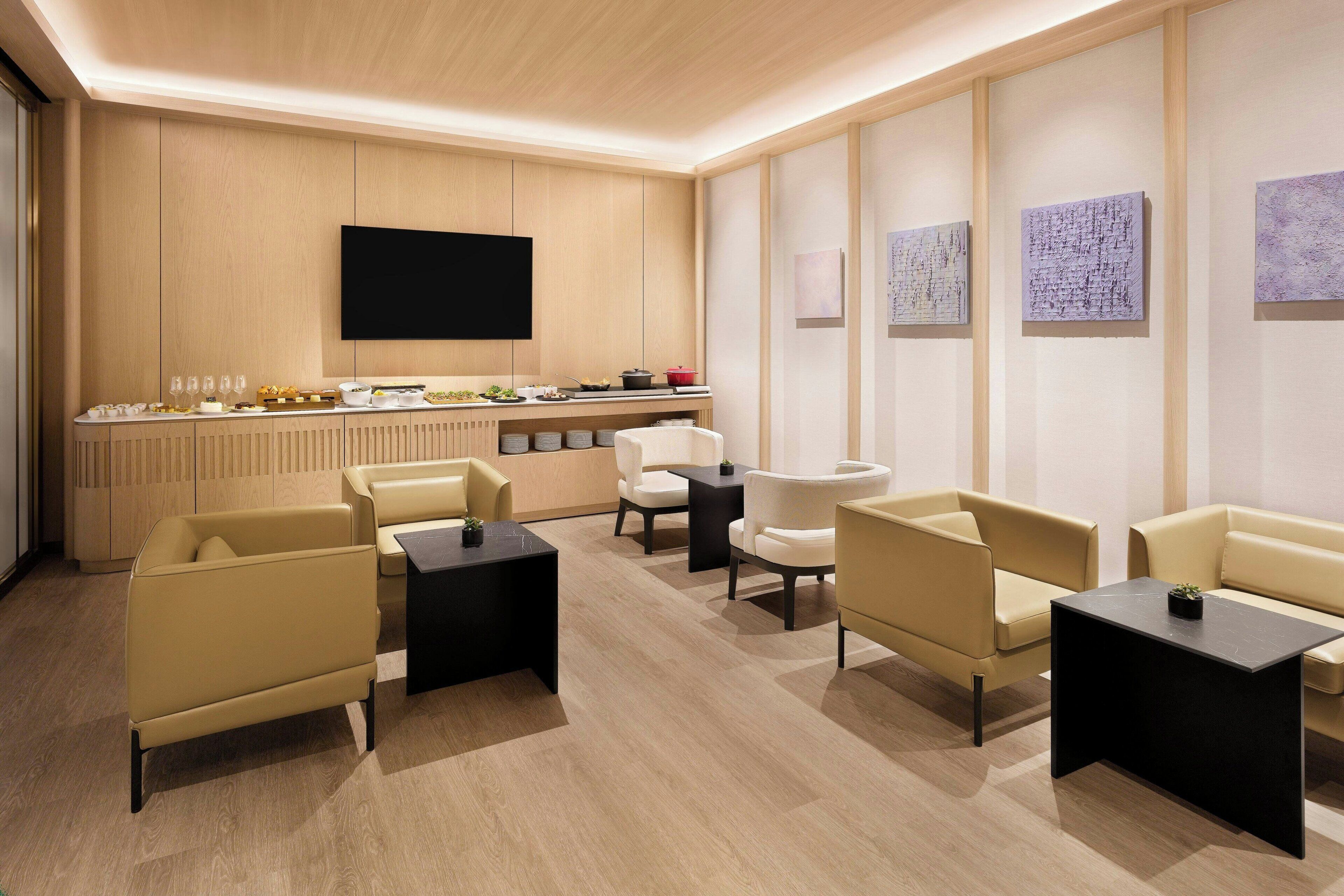 A modern lounge area with leather sofas, black side tables, and a flat-screen TV mounted on the wall.