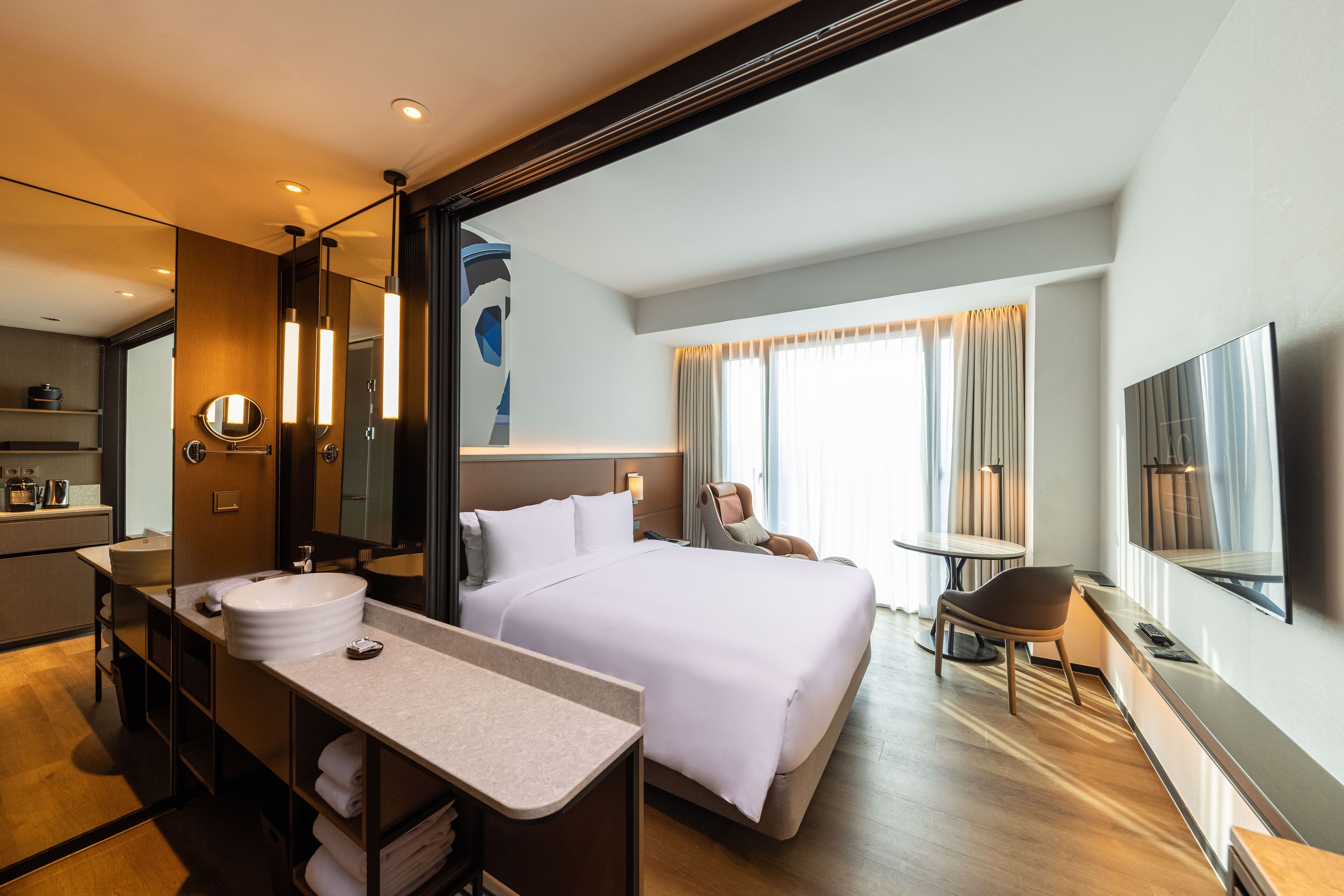 Una habitación de hotel moderna con una cama grande, un escritorio con lavamanos, una silla y un televisor.
