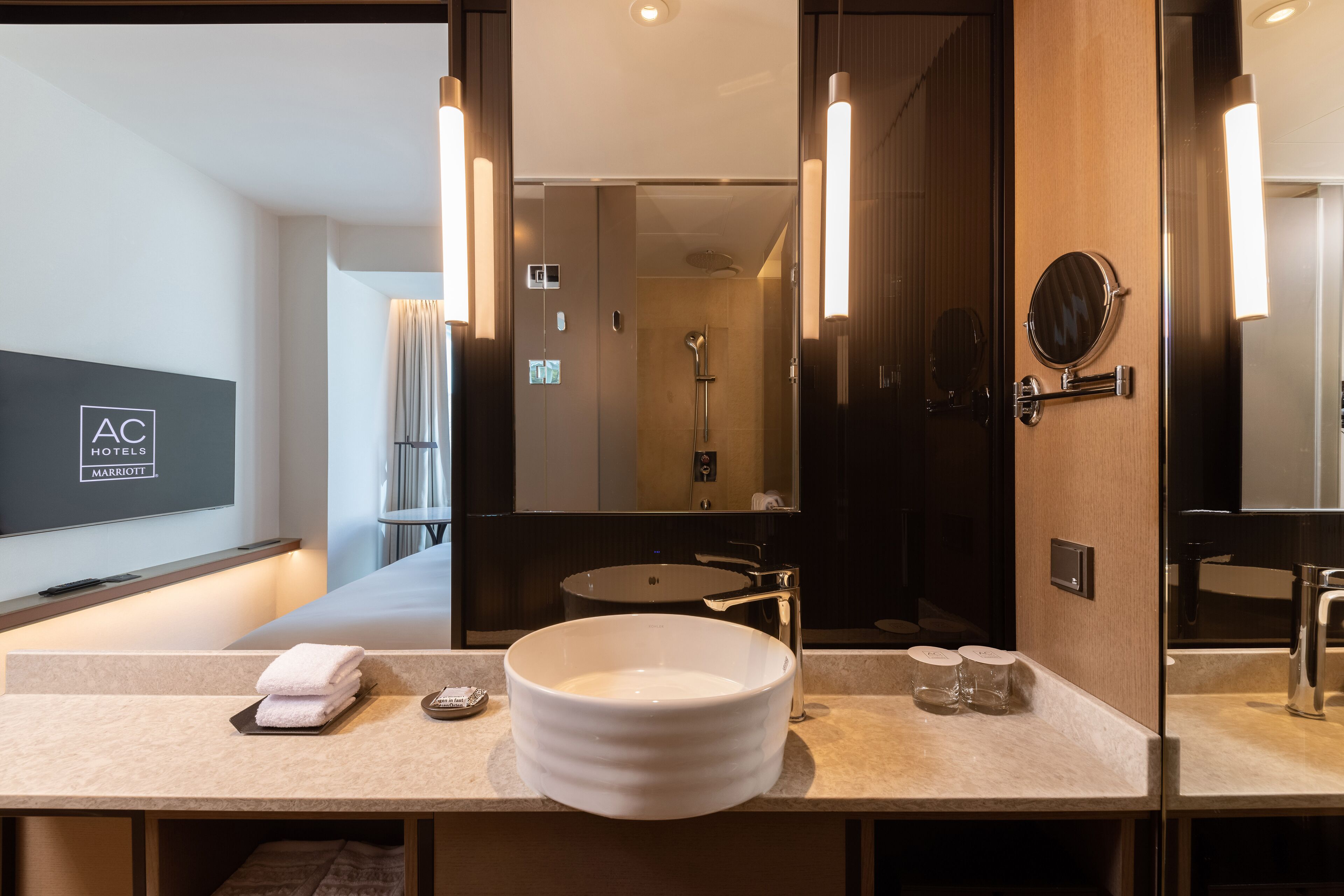 Een moderne hotelbadkamer met een grote spiegel, een rond wastafeltje en een douchehoek.