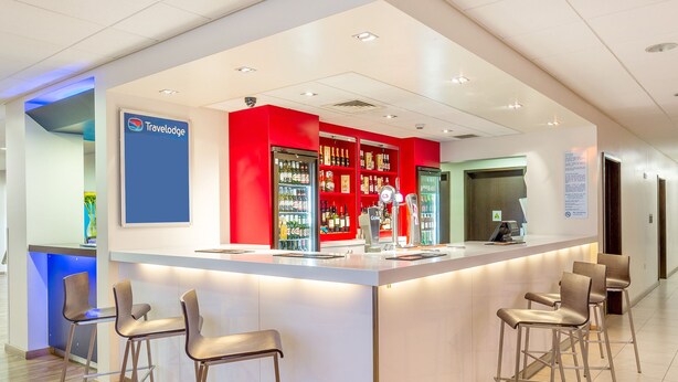 A modern reception area with a bar, seating, and a Travelodge sign. - Travelodge London Balham (London)