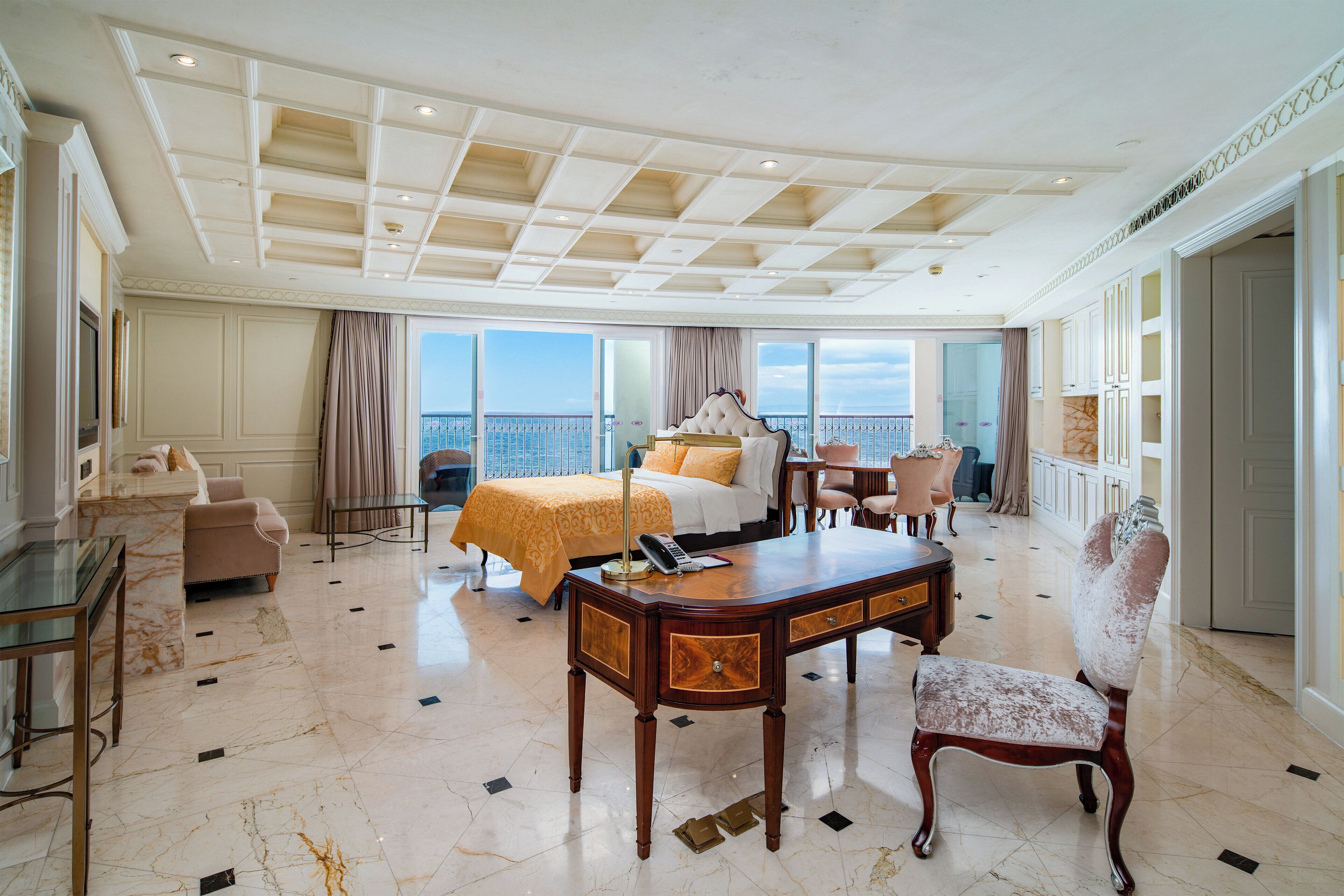 A spacious hotel room with a large bed, a desk, a chair, and a view of the city.