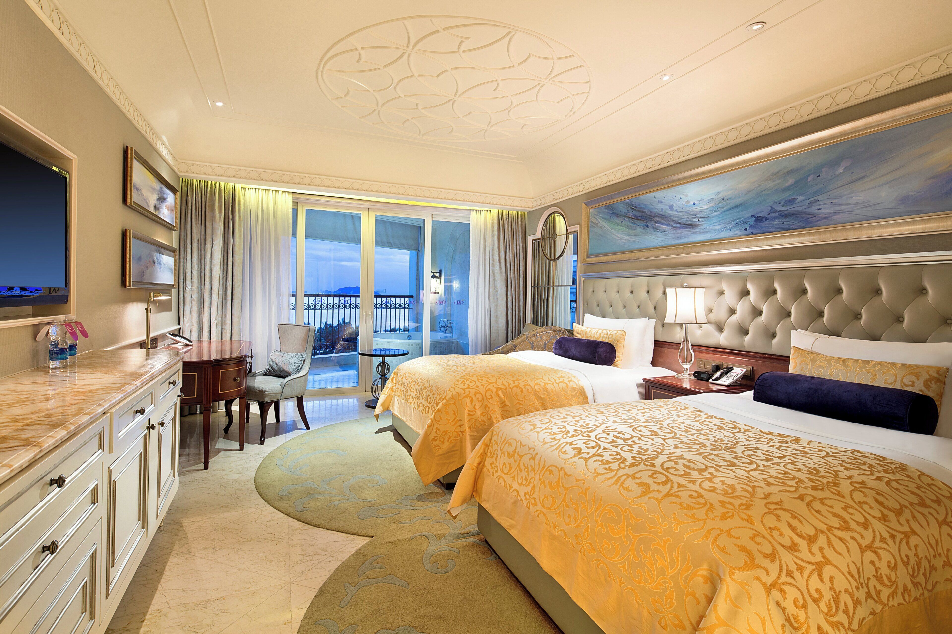 A hotel room with two beds, a sitting area, a balcony, and a painting on the wall.