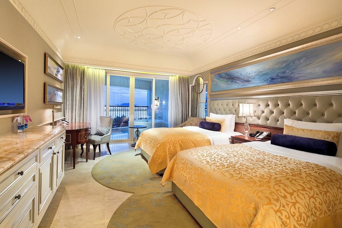 A hotel room with two beds, a sitting area, a balcony, and a painting on the wall.