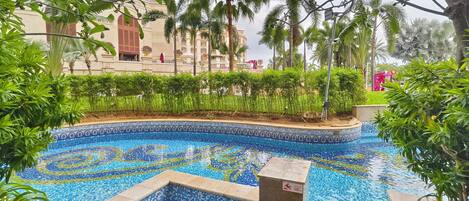A swimming pool with mosaic tiles, surrounded by lush greenery and palm trees.