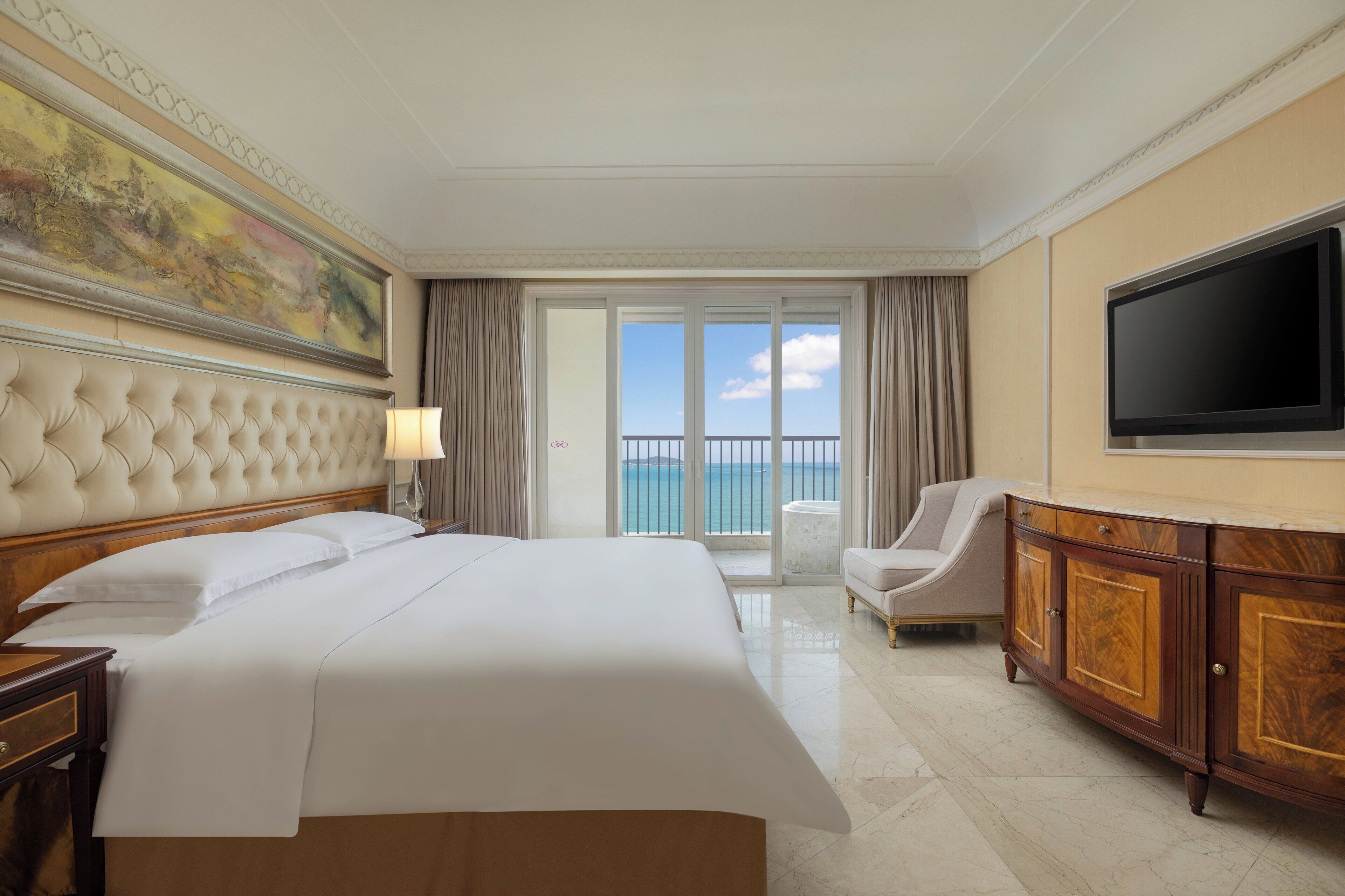A hotel room with a large bed, a TV, a balcony with a view, and a painting on the wall.