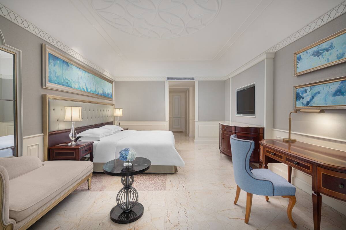 Une chambre d’hôtel équipée d’un lit, d’un bureau, d’une chaise, d’une lampe et d’œuvres d’art accrochées aux murs.