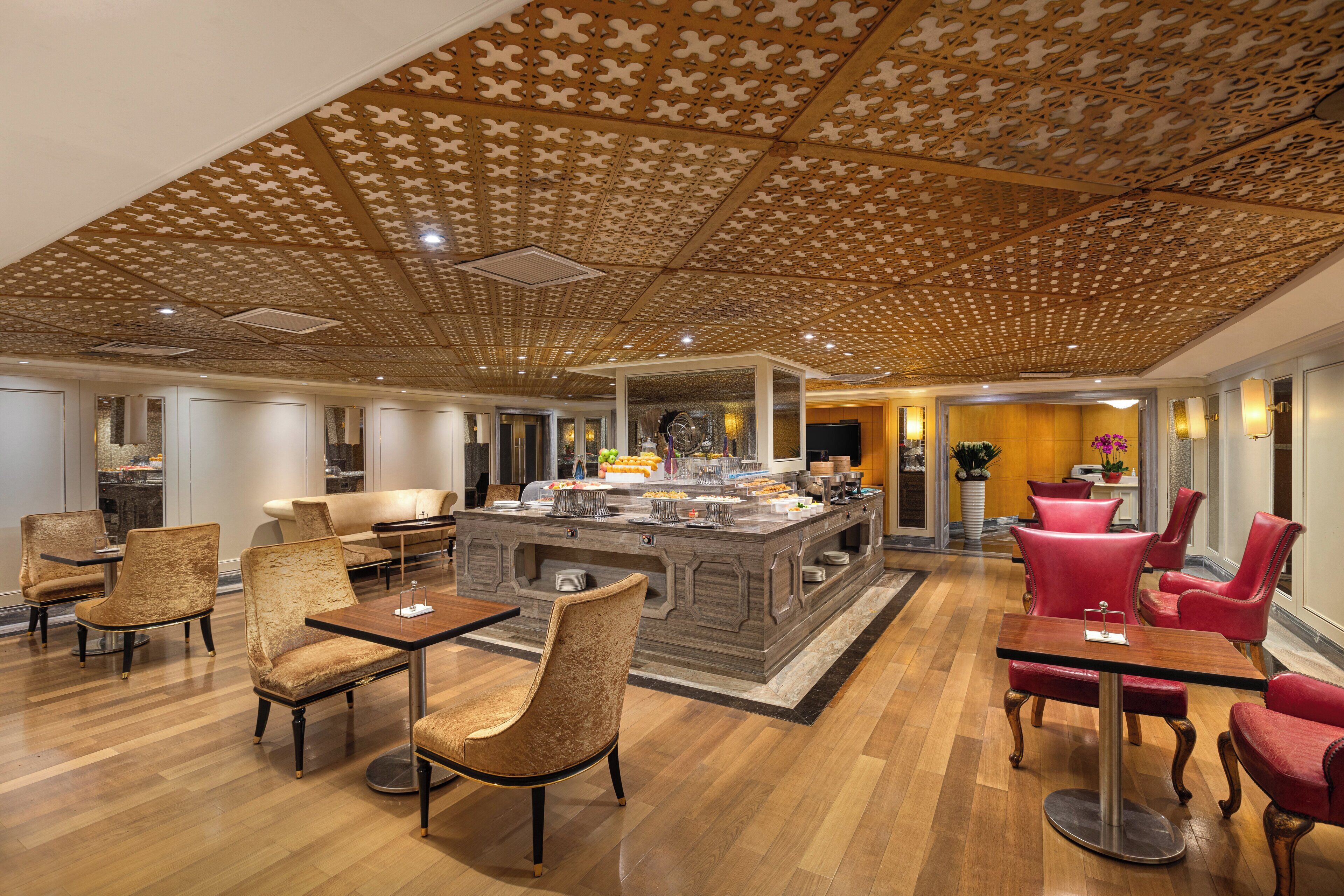 Un hall d’hôtel spacieux avec un bar central, des sièges confortables et un plafond décoratif.
