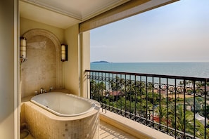Ein Badezimmer mit freistehender Badewanne, einer gefliesten Duschkabine und einem großen Fenster mit Blick auf einen Strand.