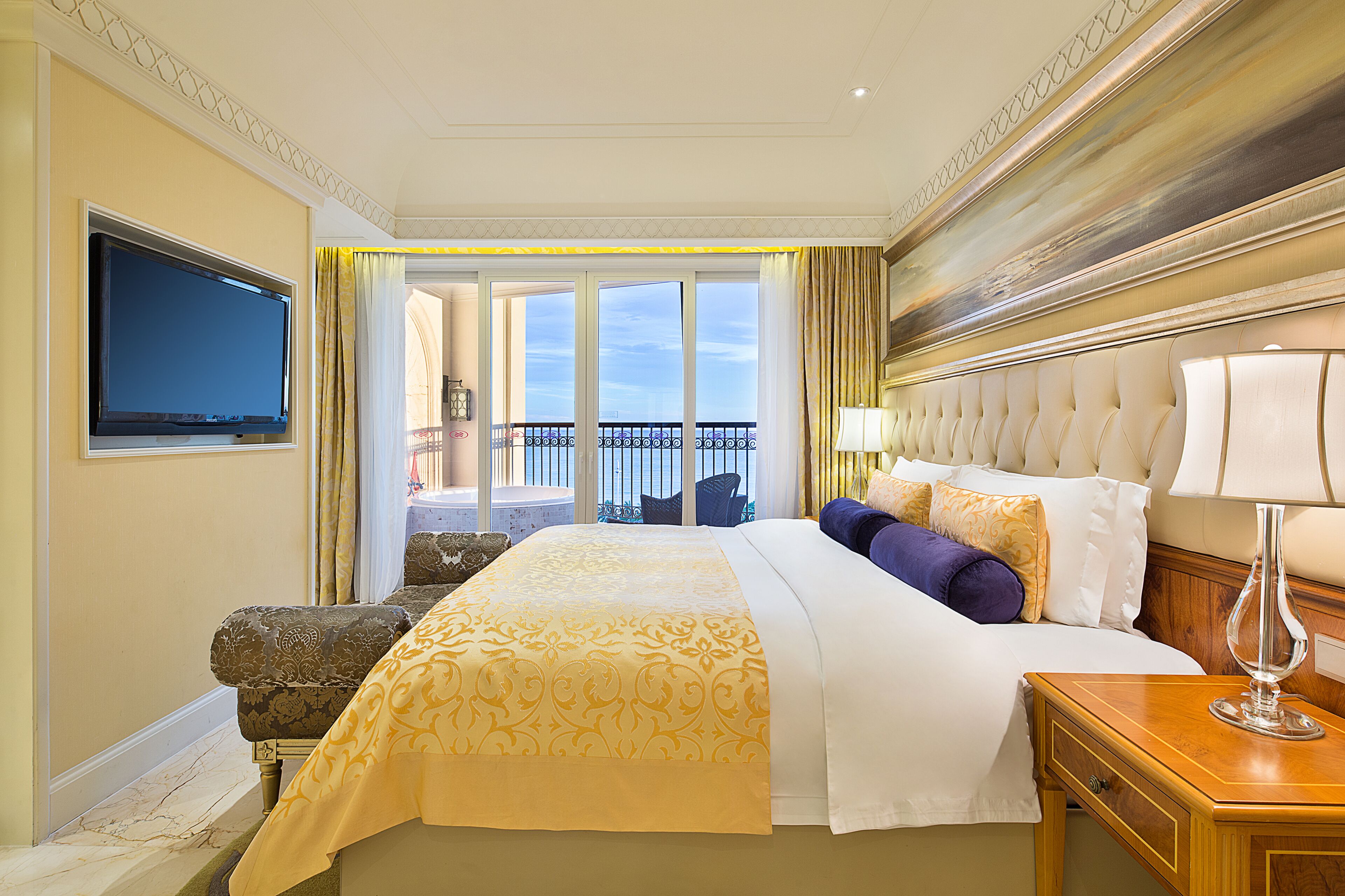 Ein Hotelzimmer mit einem großen Bett, einem Fernseher, einem Balkon mit Blick und einem Nachttisch aus Holz mit einer Lampe.