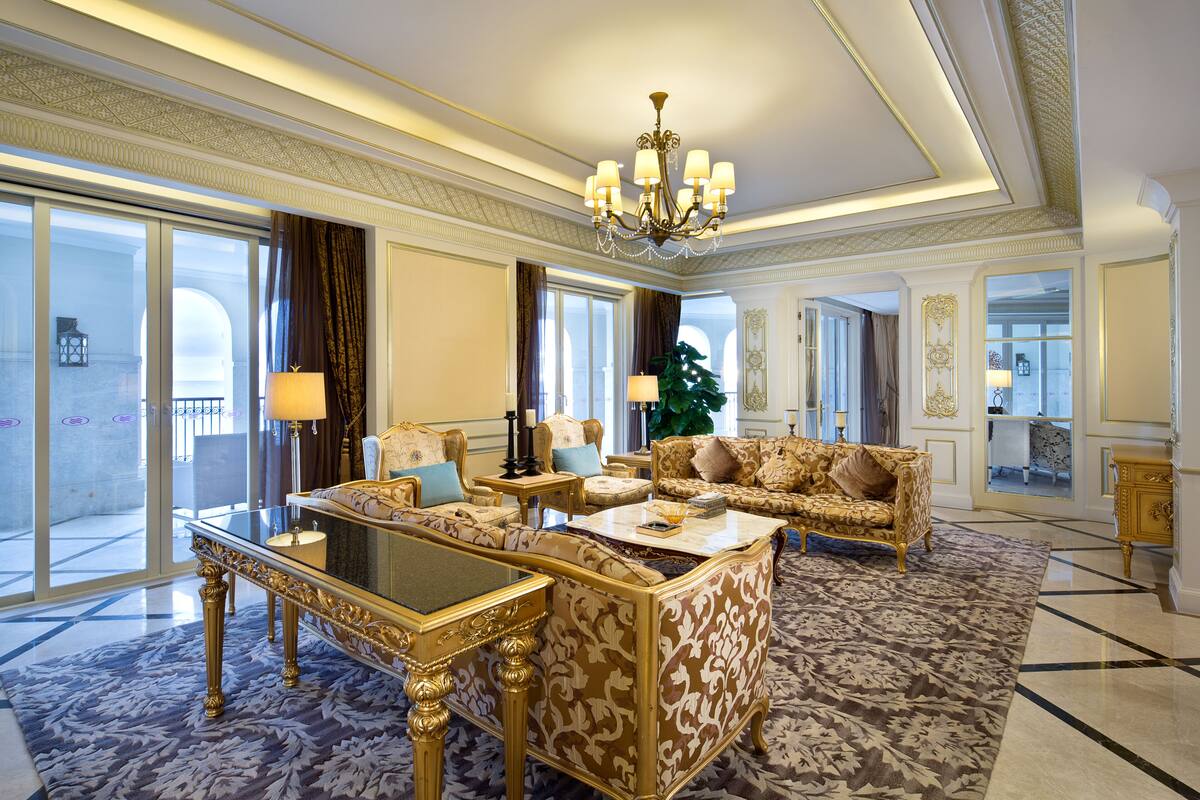 Un salon luxueux, agrémenté de meubles richement décorés, d’un lustre et de grandes fenêtres offrant une vue imprenable.