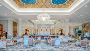 Un vaste hall d’entrée agrémenté d’un plafond richement décoré, d’un lustre et de coins salons luxueux.