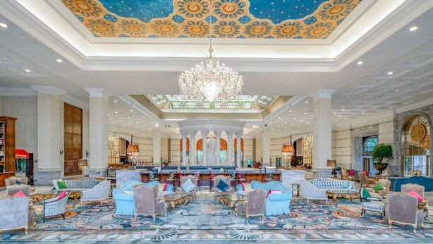 Un vaste hall d’entrée agrémenté d’un plafond richement décoré, d’un lustre et de coins salons luxueux.
