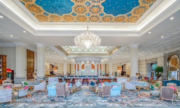 A grand lobby with ornate ceiling, a chandelier, and luxurious seating areas.