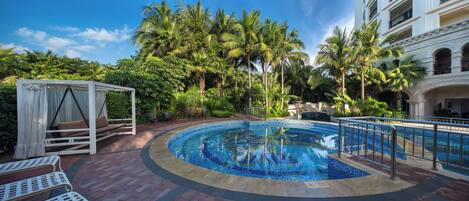 A pool area with a circular design, surrounded by palm trees and a white gazebo.