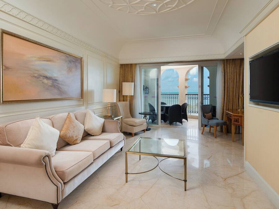 A spacious living room with a beige sofa, a glass coffee table, and a large painting on the wall.