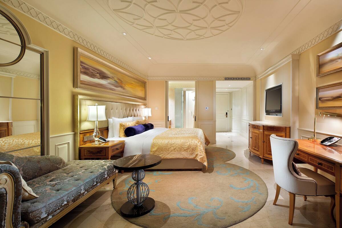 Une chambre d’hôtel avec un lit, un canapé, un bureau, une télévision et une salle de bain visible à travers une porte ouverte.