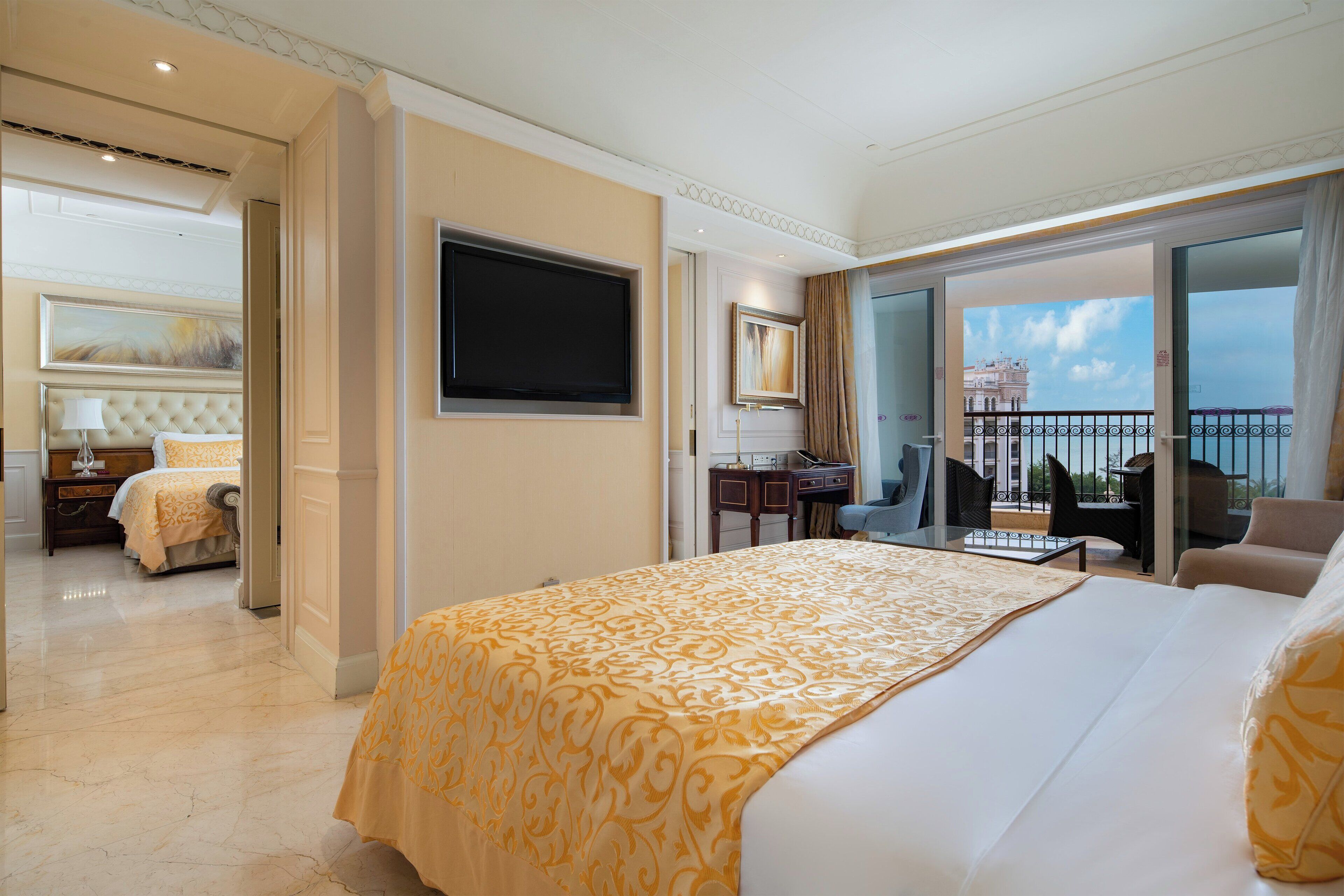 A hotel room with a large bed, a TV, a desk, and a balcony with a view of a building.