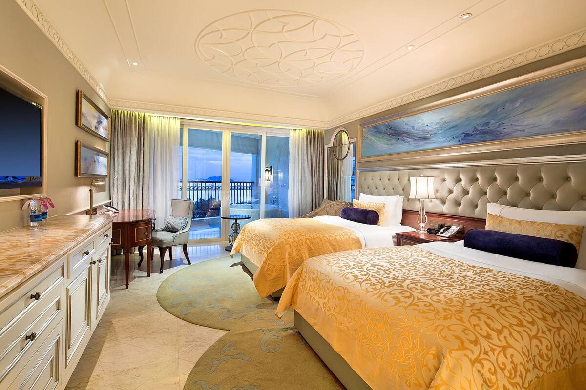 Une chambre d’hôtel avec deux lits, un grand tableau, un balcon avec vue et un bureau avec une chaise.