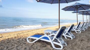 A beach with rows of sun loungers and striped umbrellas.