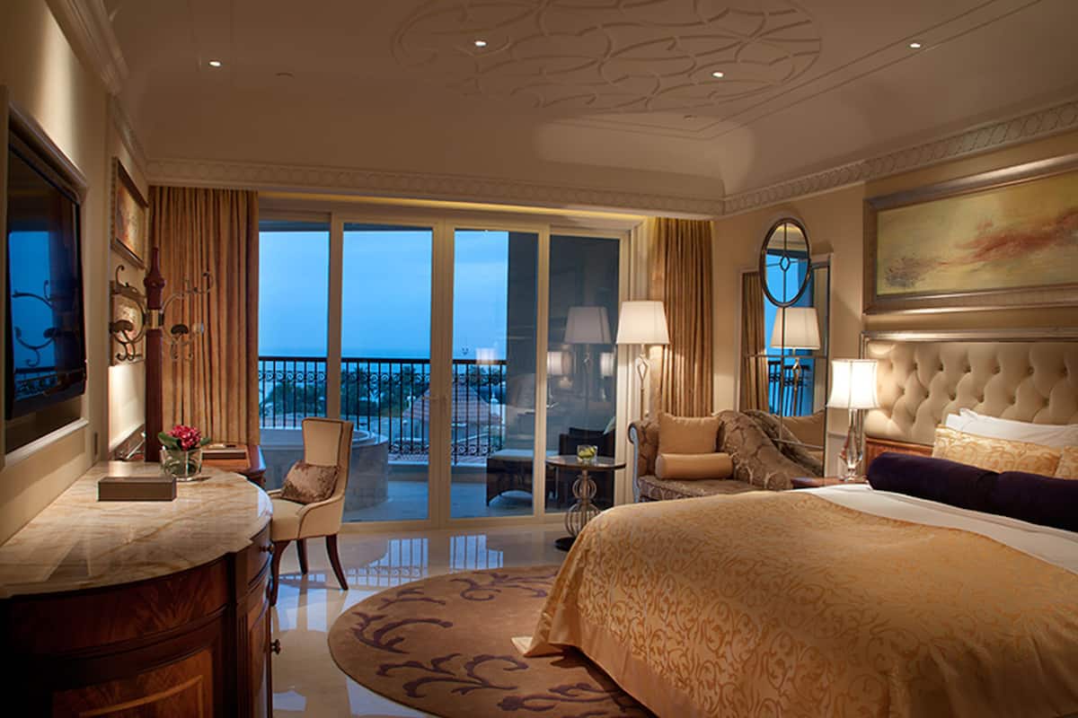 Une chambre d’hôtel dotée d’un grand lit, d’un coin salon avec un fauteuil et une table, d’un balcon avec vue et d’un grand tableau accroché au mur.