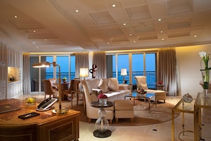A spacious hotel living room with a large sofa, armchairs, a coffee table, and a desk with a telephone.