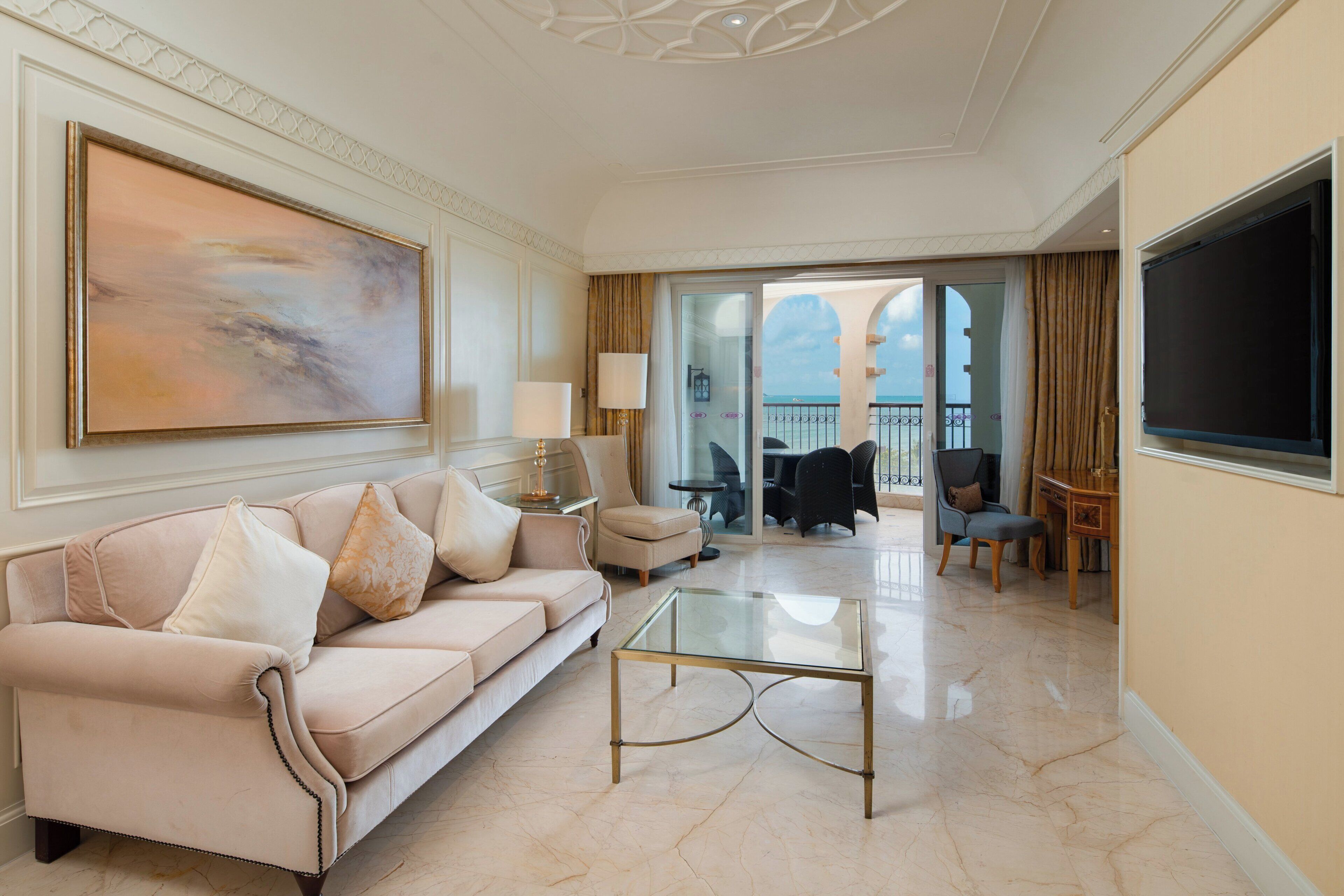 A spacious living room with a beige sofa, a glass coffee table, and a large painting.