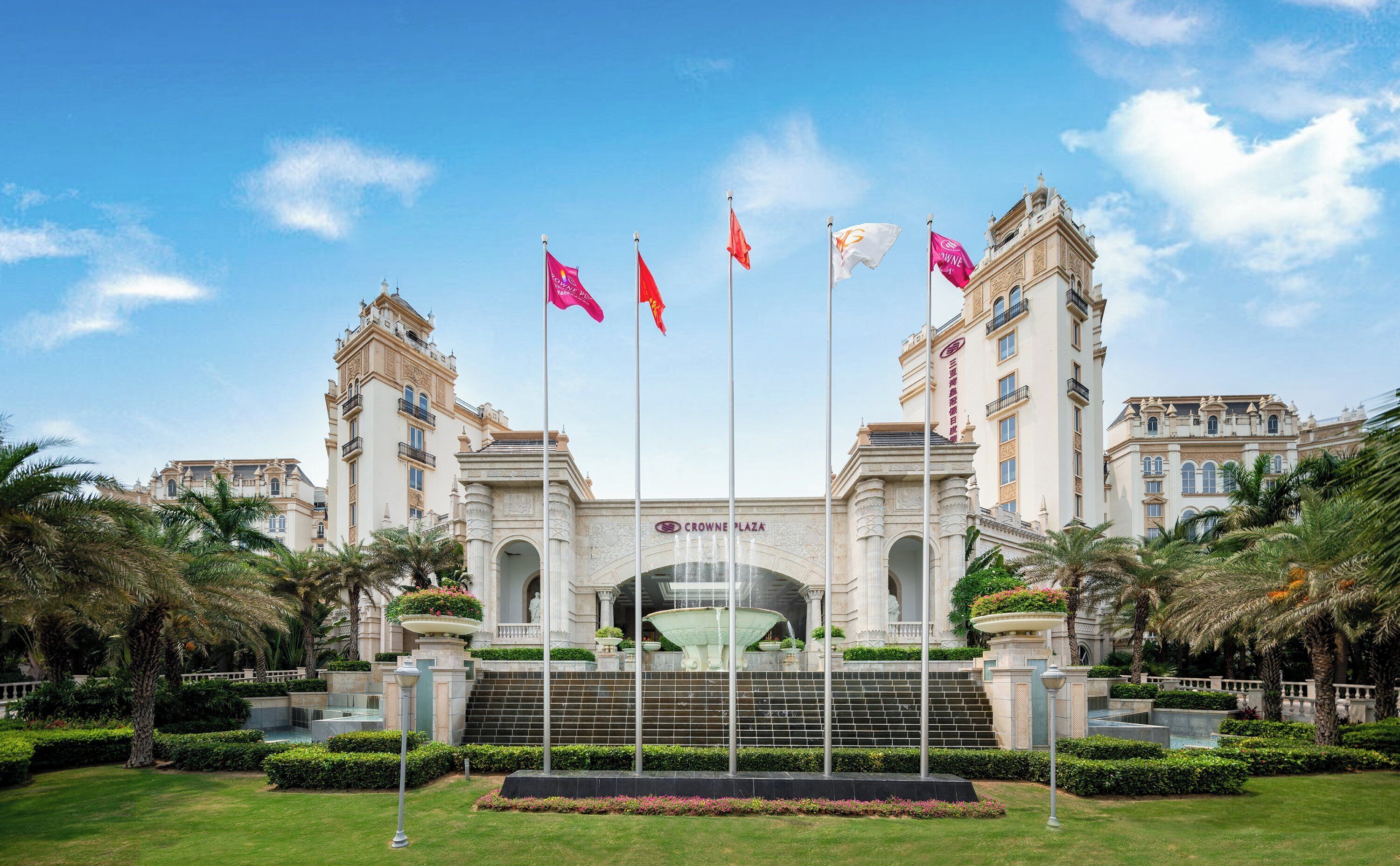 A grand hotel entrance with a central fountain, multiple flags, and classical architecture.
