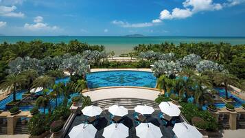 A resort pool area with multiple swimming pools, surrounded by palm trees and a view of the ocean.