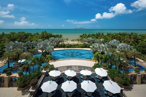 Ein Poolbereich eines Resorts mit mehreren Schwimmbecken, umgeben von Palmen und Blick auf den Ozean.