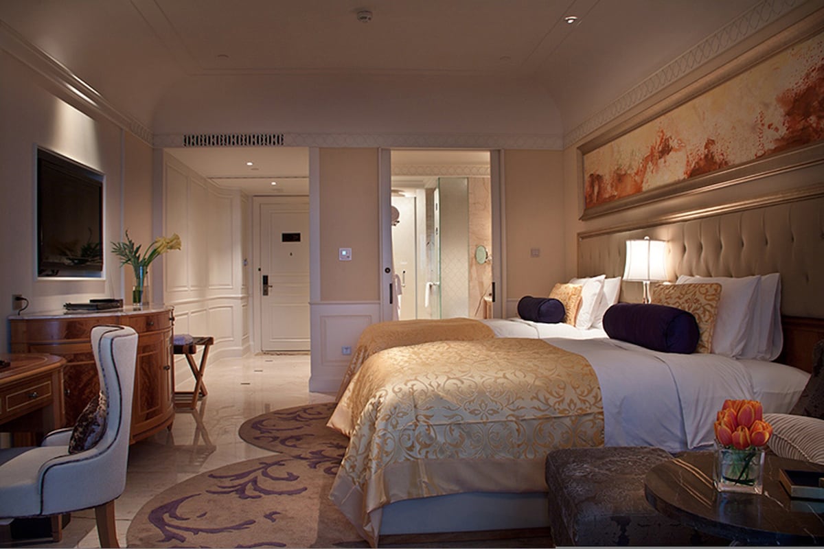 A hotel room with a bed, a desk, a chair, a television, and a painting on the wall.